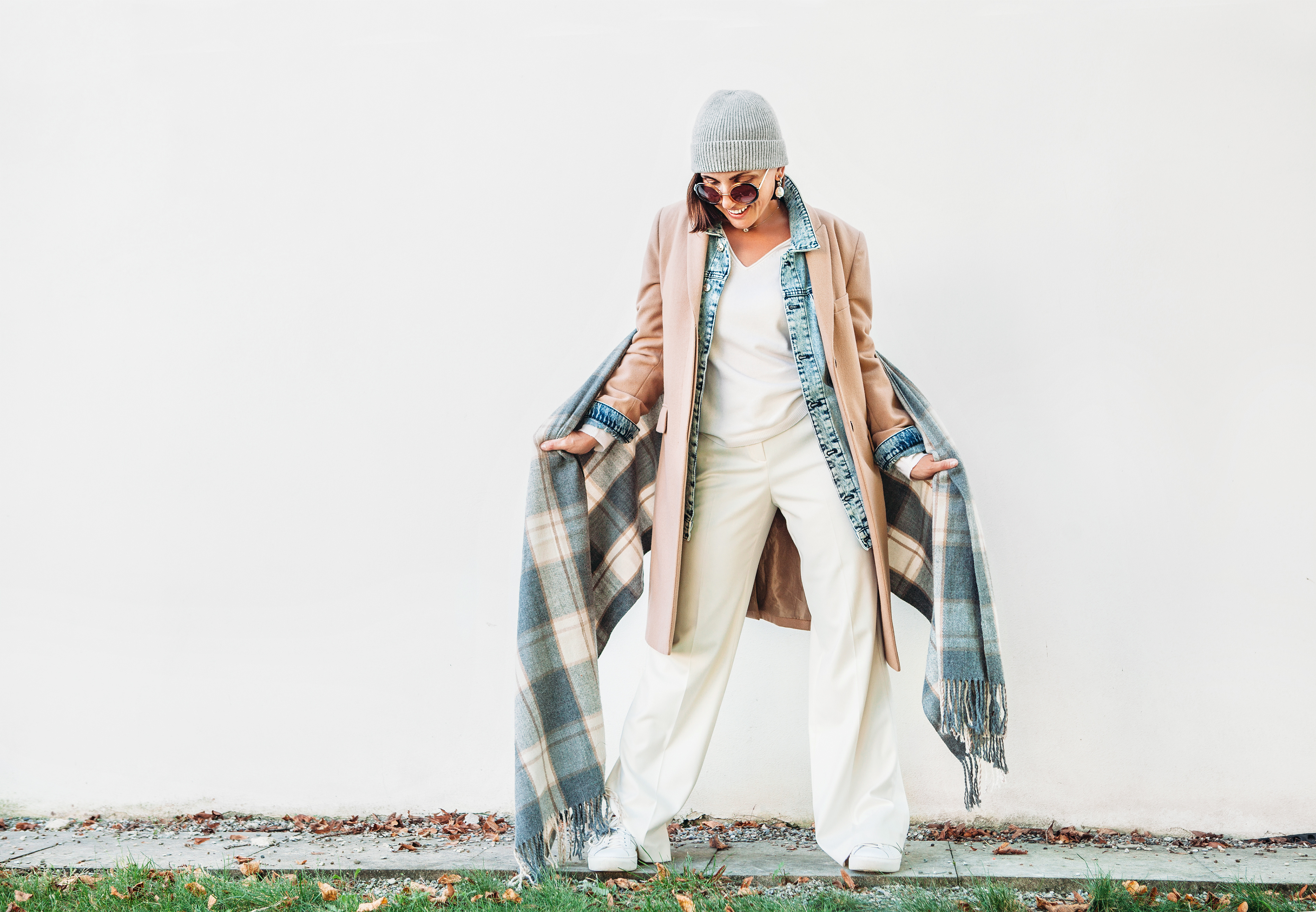 Woman dressed in multilayered autumn outfit: camel coat, denim jacket and elegant trousers