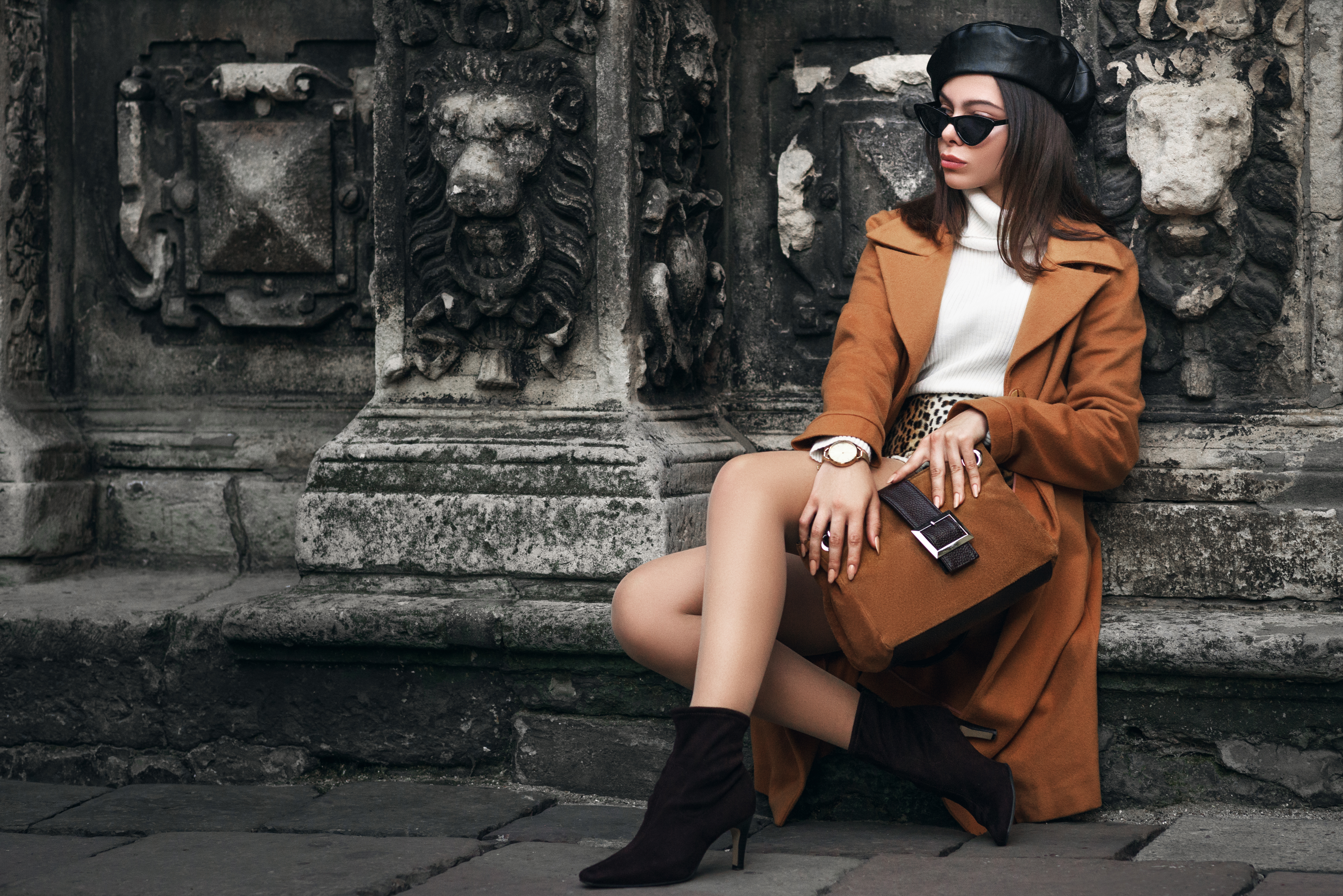 Outdoor full body fashion portrait of elegant woman wearing glasses, beret, wrist watch, turtleneck, coat, ankle boots, holding suede handbag, posing in street of european city. Copy, empty space