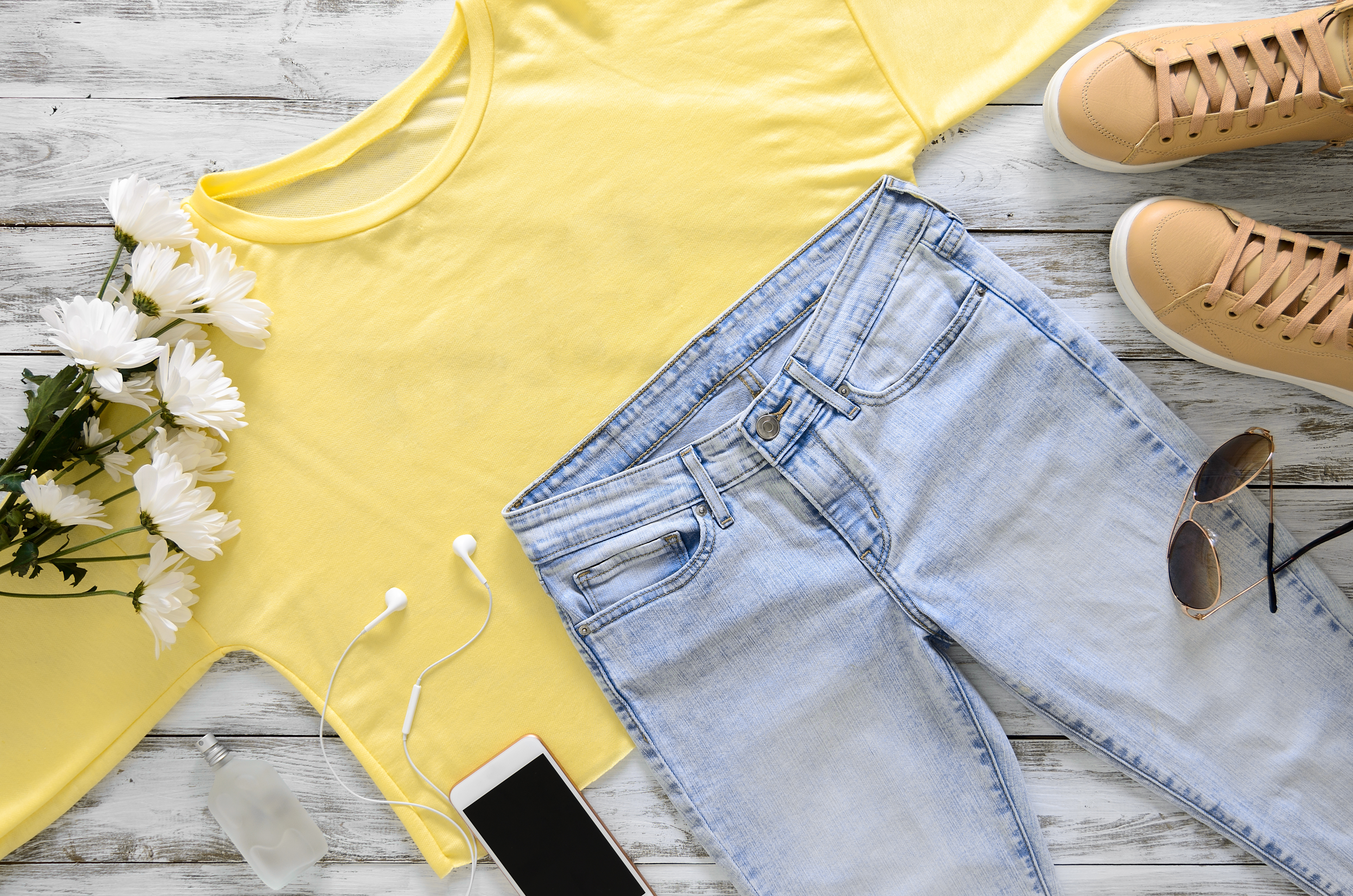 Womens fashion clothing, shoes and accessories (beige leather sneakers, blue jeans, yellow top (long sleeve t-shirt) headphones, cell phone, perfume, sunglasses. Fashion concept. View from above, Flat lay. Spring summer season